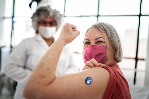 Vaccinated senior woman flexing biceps muscle with 'Got vaccinated' sticker on - wearing face mask