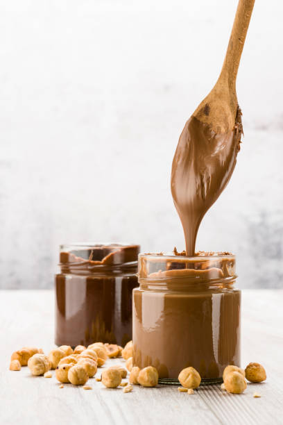 Chocolate cream Chocolate cream in glass jar with hazelnuts and dripping spoon, on wooden table jar of milk stock pictures, royalty-free photos & images