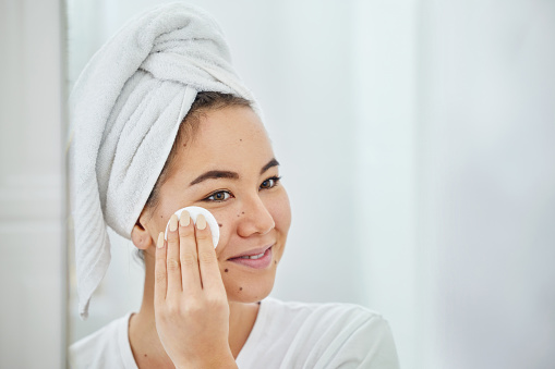 Foto de una joven que se limpia la cara con una almohadilla de algodón en un baño de casa photo