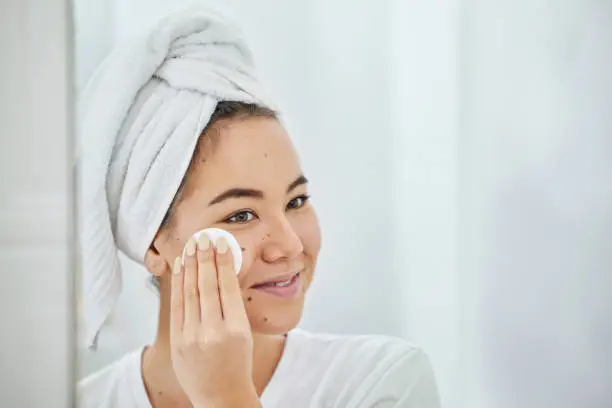 Photo of Shot of a young woman cleaning her face with a cotton pad in a bathroom at home