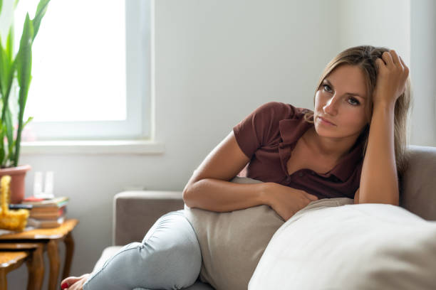 Sad woman sitting on sofa alone at home Sad woman sitting on sofa alone at home unwanted pregnancy stock pictures, royalty-free photos & images