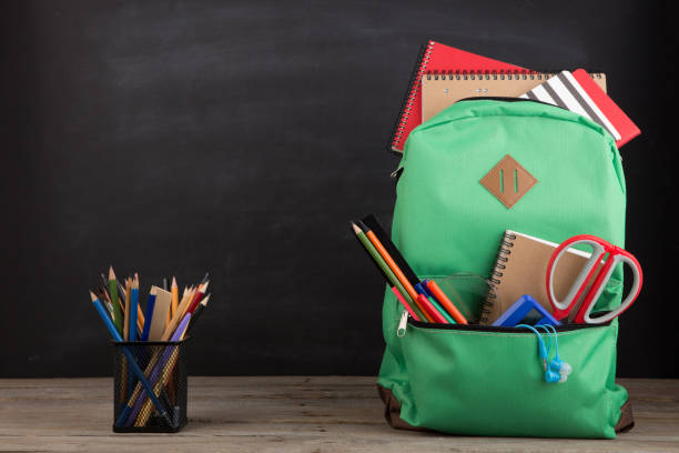 istock Education concept - school backpack with books and other supplies, blackboard background 1330731603