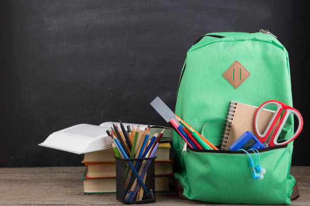 istock Education concept - school backpack with books and other supplies, blackboard background 1330732326
