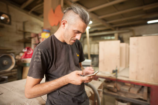 istock Carpenter artisan resting in workshop and scrolling on smartphone 1330735983