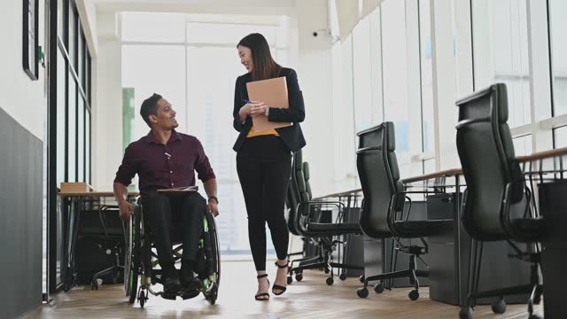 Indian Businessman in wheelchair walking with female colleague  discussing  at workplace