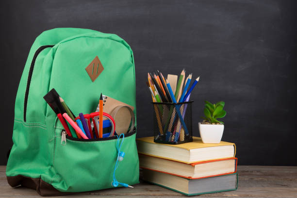 istock Education concept - school backpack with books and other supplies, blackboard background 1330736119