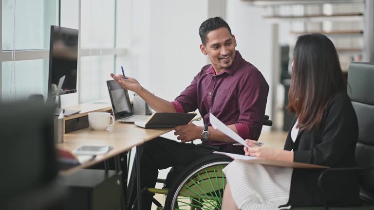 Indian Businessman in wheelchair having discussion with his female Chinese colleague in creative office