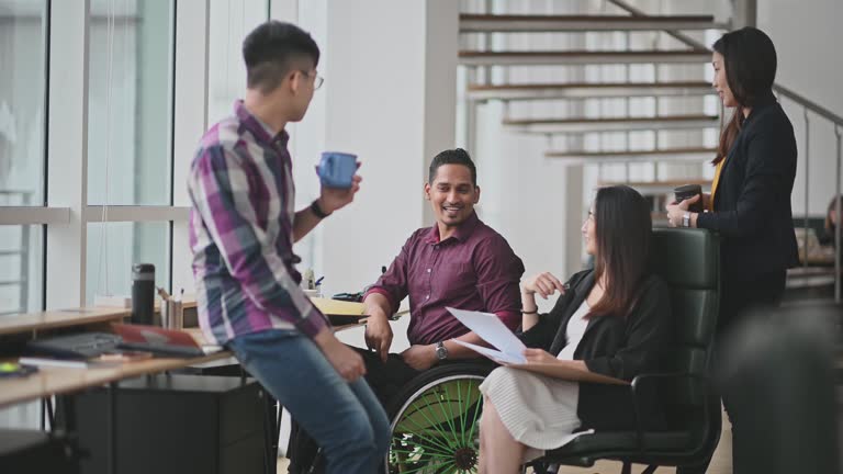 Indian Businesssman in wheelchair leading group discussion in creative office