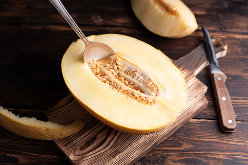 Spoon in the seeds of half a ripe melon on a cutting board on a dark wooden background, healthy food.