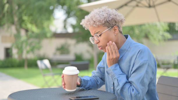 African Woman having Toothache in Outdoor Cafe Young African Woman having Toothache in Outdoor Cafe Tooth Infection stock pictures, royalty-free photos & images