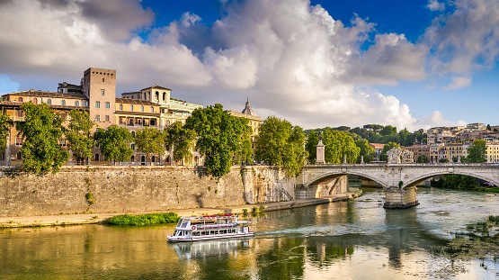 A ferry boat sails along the Tiber River in the light of the sunset in the heart of Rome