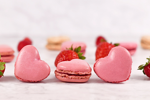 Round baked multicolored macarons lie in a red heart shaped box on wooden background