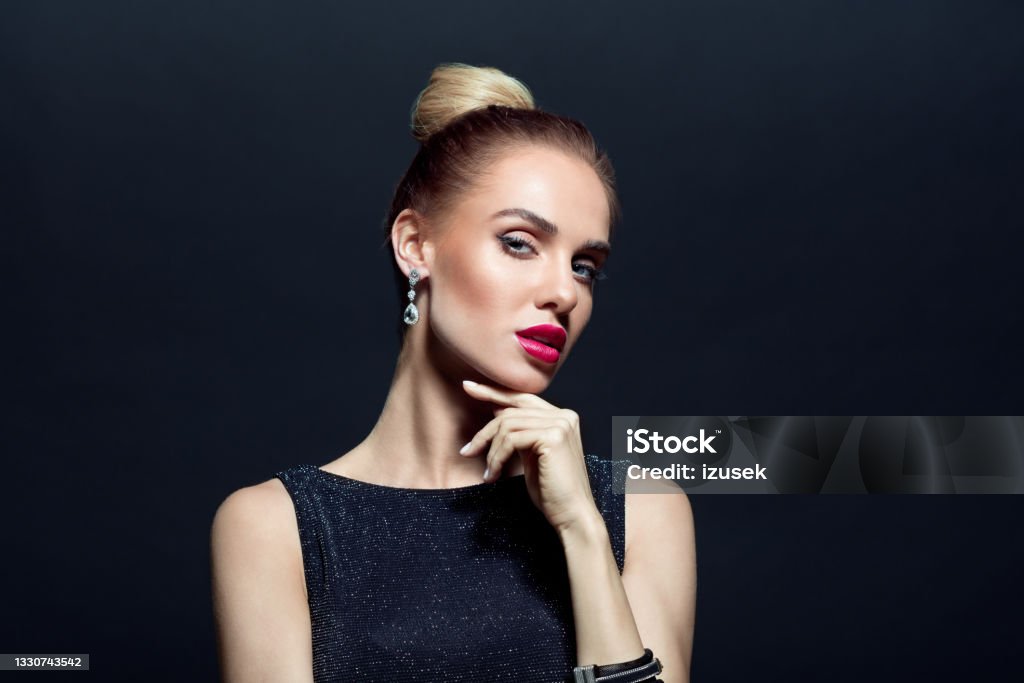 Portrait of beautiful woman on back background Headshot of elegant, beautiful woman wearing black evening gown and earrings looking at camera. Close up of face. Studio shot against black background. Fashion Model Stock Photo