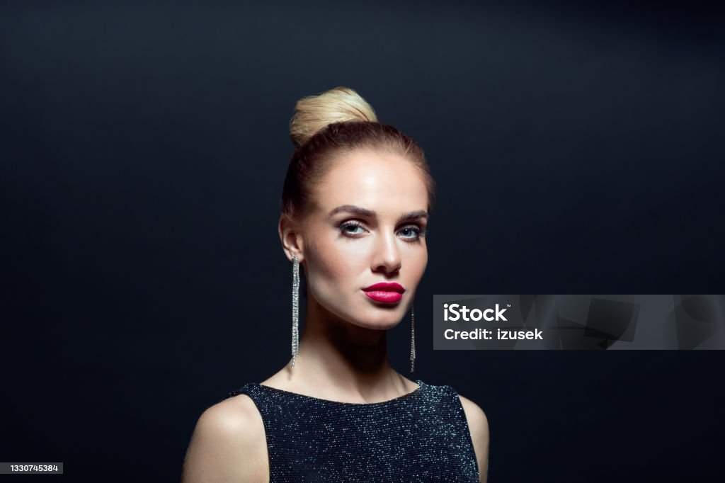Portrait of beautiful woman on back background Headshot of elegant, beautiful woman wearing black evening gown and earrings looking at camera. Close up of face. Studio shot against black background. 20-29 Years Stock Photo