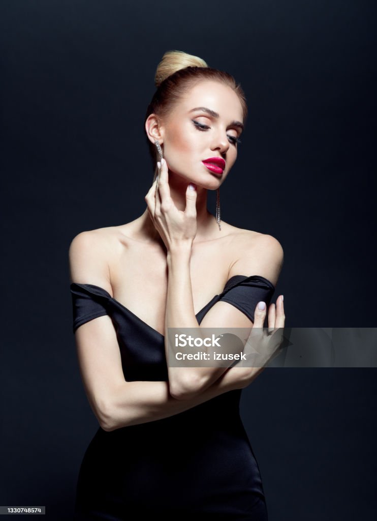 Portrait of elegant woman on back background Beautiful woman wearing black evening gown and earrings. Studio shot against black background. Beautiful Woman Stock Photo