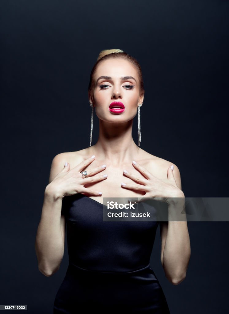 Portrait of elegant woman on back background Beautiful woman wearing black evening gown and earrings, looking at camera.  Studio shot against black background. 20-29 Years Stock Photo