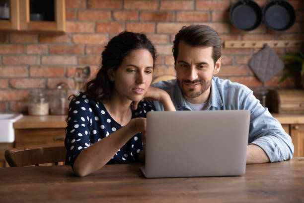 istock Happy millennial couple using laptop in kitchen, watching show together 1330750313