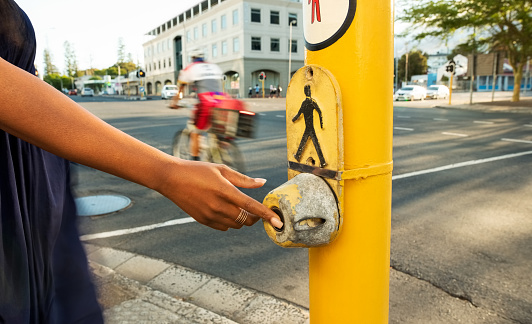 Close-up of a woman hand pushing a pedestrian traffic light button to request a change in the lights for crossing road safely