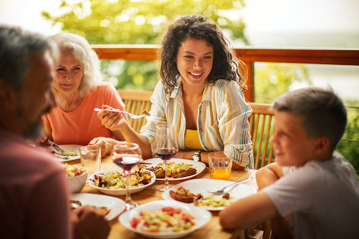 Family dinner, happy woman and salad with children at home for nutrition. Celebration, together and people with kids eating at table with happiness and a smile in a house giving lunch on plate