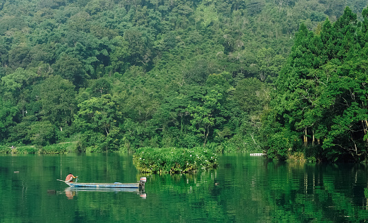 Sun Moon Lake (A well-known tourist attraction in Taiwan),
A lake full of green surrounded by forest, A fisherman handles his fishing tackle on his boat.