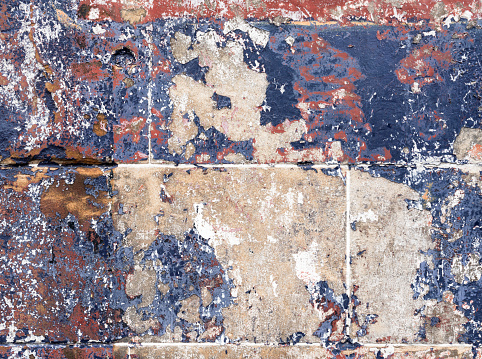 A macro image showing layers of red, blue and white faded and weathered to reveal exposed stone on an exterior wall surface.