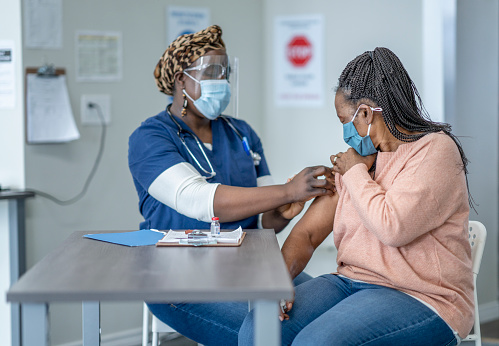 A nurse administers a dose of the vaccine to a middle aged woman in the clinic.