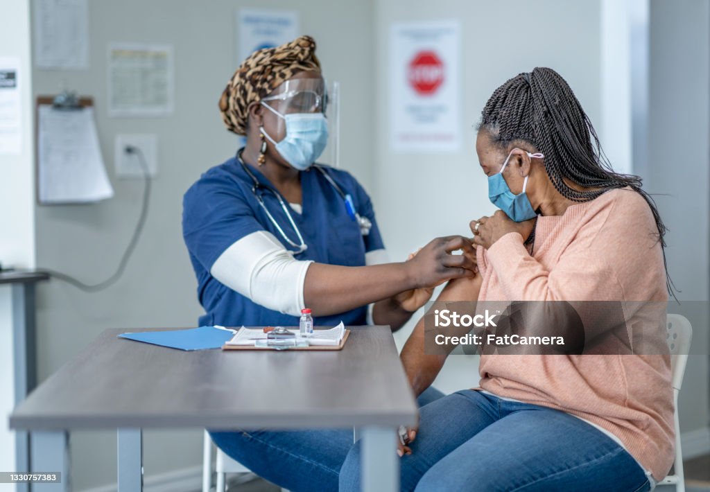 Vaccination clinic A nurse administers a dose of the vaccine to a middle aged woman in the clinic. Vaccination Stock Photo