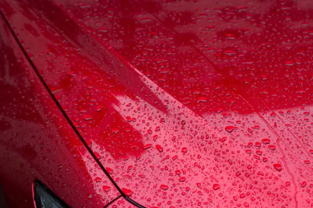The surface of the car in raindrops. The red car is covered with water from precipitation.