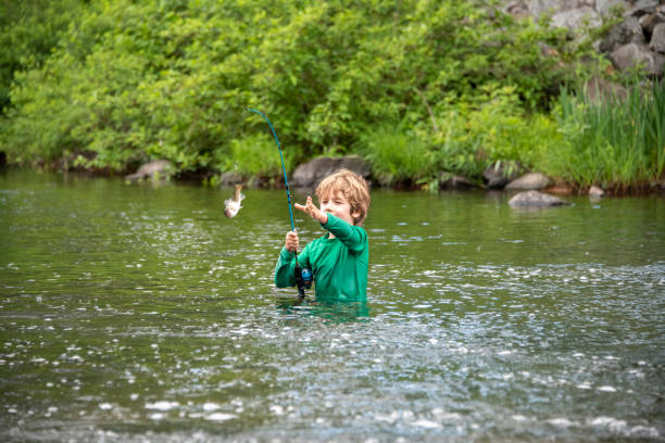 Young boy reels in a fish A young boy works to reel in a trout on his own. He is fishing where Red Bridge Dam empties Lake Rescue into Lake Pauline in Vermont. trout lake stock pictures, royalty-free photos & images