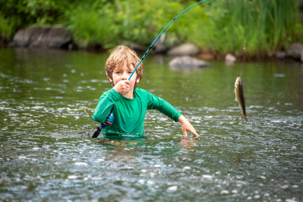 young boy reels in a fish - trout fishing imagens e fotografias de stock