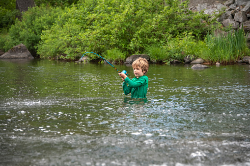 A young boy works to reel in a trout on his own. He is fishing where Red Bridge Dam empties Lake Rescue into Lake Pauline in Vermont.