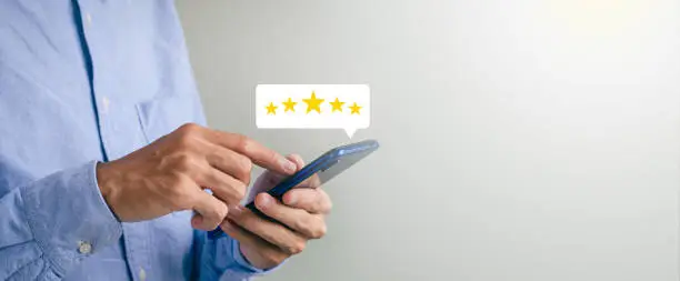 Photo of Businessman press close-up button on smartphone screen with golden light star icon and cool star gradation to get best score. Can be used in technology business