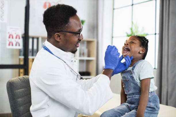 afro-american child girl at doctor's office, handsome black male doctor examining her throat - doctor patient male tongue depressor imagens e fotografias de stock
