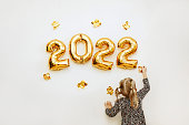 Little girl decorates the wall of the house with golden numbers 2022