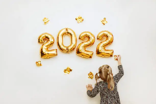 Photo of Little girl decorates the wall of the house with golden numbers 2022