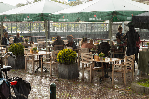 Tourists take shelter under the umbrellas of a terrace from the rain in the center of Muiden in the Netherlands