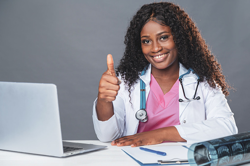 African american smiling female doctor sitting at the table in the medical office and working on the computer, telemedicine, online patient consultation