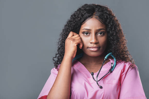 istock Tired exhausted african nurse in pink uniform on gray background 1330769682