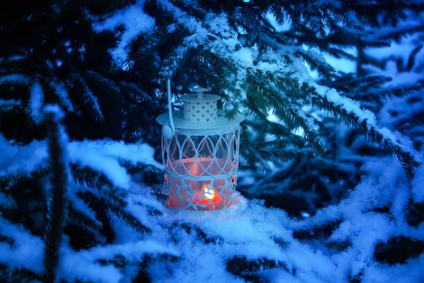 istock Decorative Christmas lantern with burning candle hanging on snow-covered fir- tree branch in a winter park. New year festive card, poster, postcard design. 1330772456