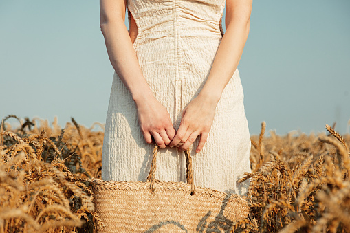 View on white woman in a dress holding bag on wheat field
