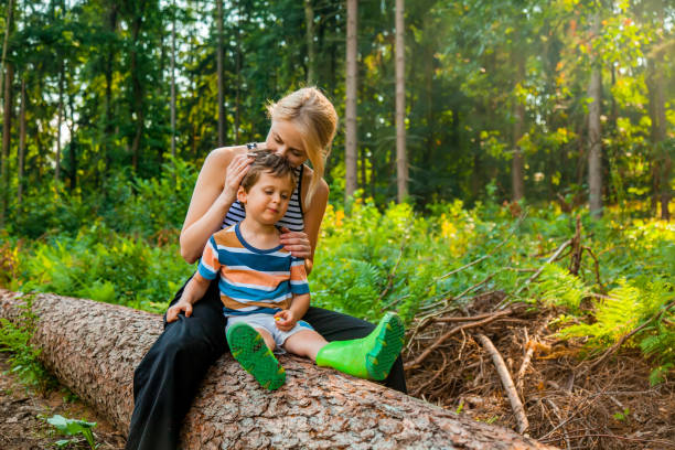 istock Beautiful blond hair mothe sits on log with son in forest 1330772589