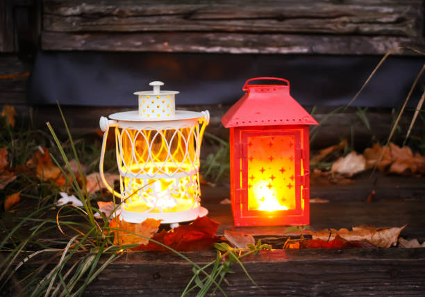 Decorative lanterns with burning candles on old wooden threshold of rural bathhouse in autumn park at evening.