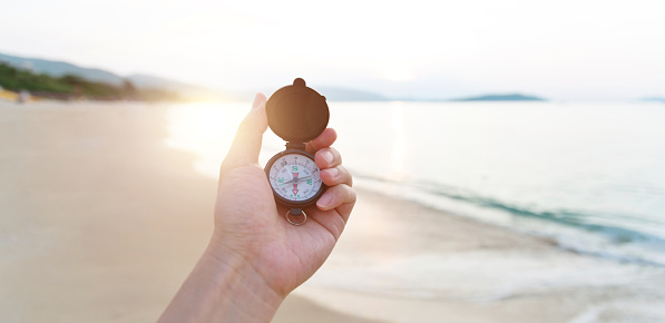 Human hand holding a compass by the sea.