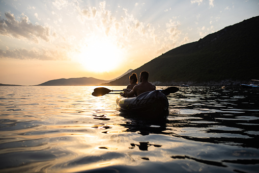 An attractive young couple is having fun kayaking at the sea at sunset