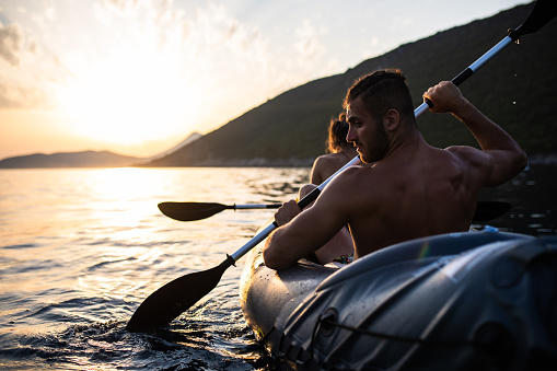 An attractive young couple is having fun kayaking at the sea at sunset