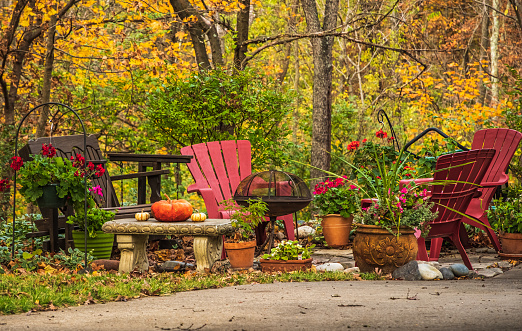 View of group of chairs, grill and potted plants in Midwestern front yard in autumn; red maples in background