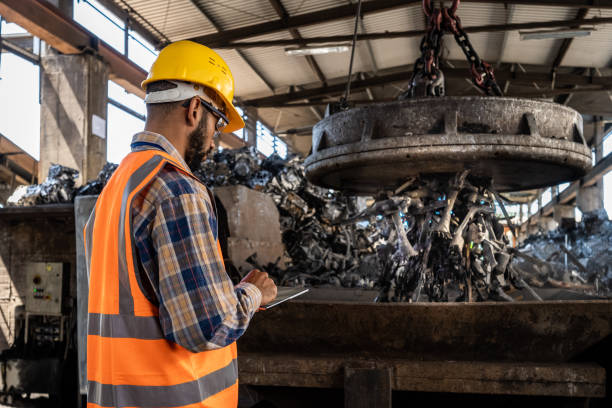 Man making notes to digital tablet. Huge magnet used for iron waste transport in background.