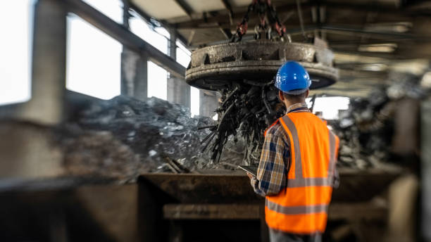 Back view of man looking at electro magnet transporting in iron scrap hall.
