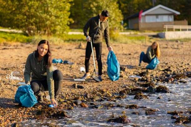 istock Young woman in a team picking up plastic garbage in bag at beach 1330784066