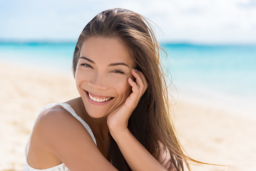 Healthy beautiful Asian multiracial woman on beach. Portrait of pretty Chinese Caucasian mixed race brunette girl in her 20s relaxing on summer vacations. Confident and modern young adult.
